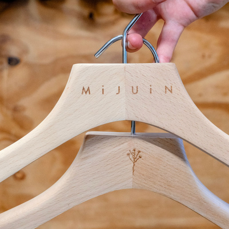 Deux cintres en bois gravés avec le nom Mijuin et un motif floral, tenus à la main.
