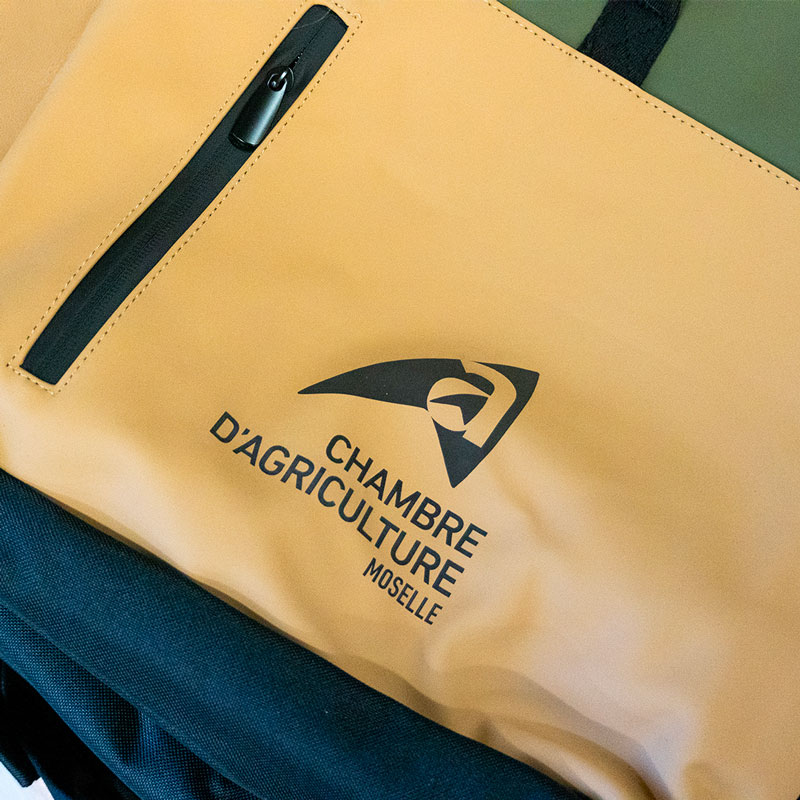 Gravure laser sur textile : logo Chambre d’agriculture de Moselle sur la poche jaune d’un sac à dos.
